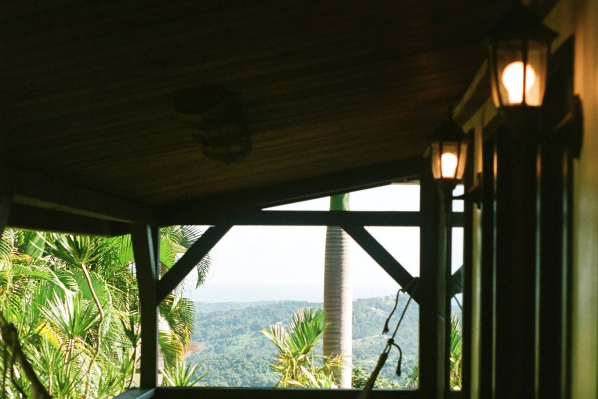 La véranda en bois du gîte : un hamac de coton, deux lanternes allumées, et la vue sur les palmiers, les mornes et la mer au loin