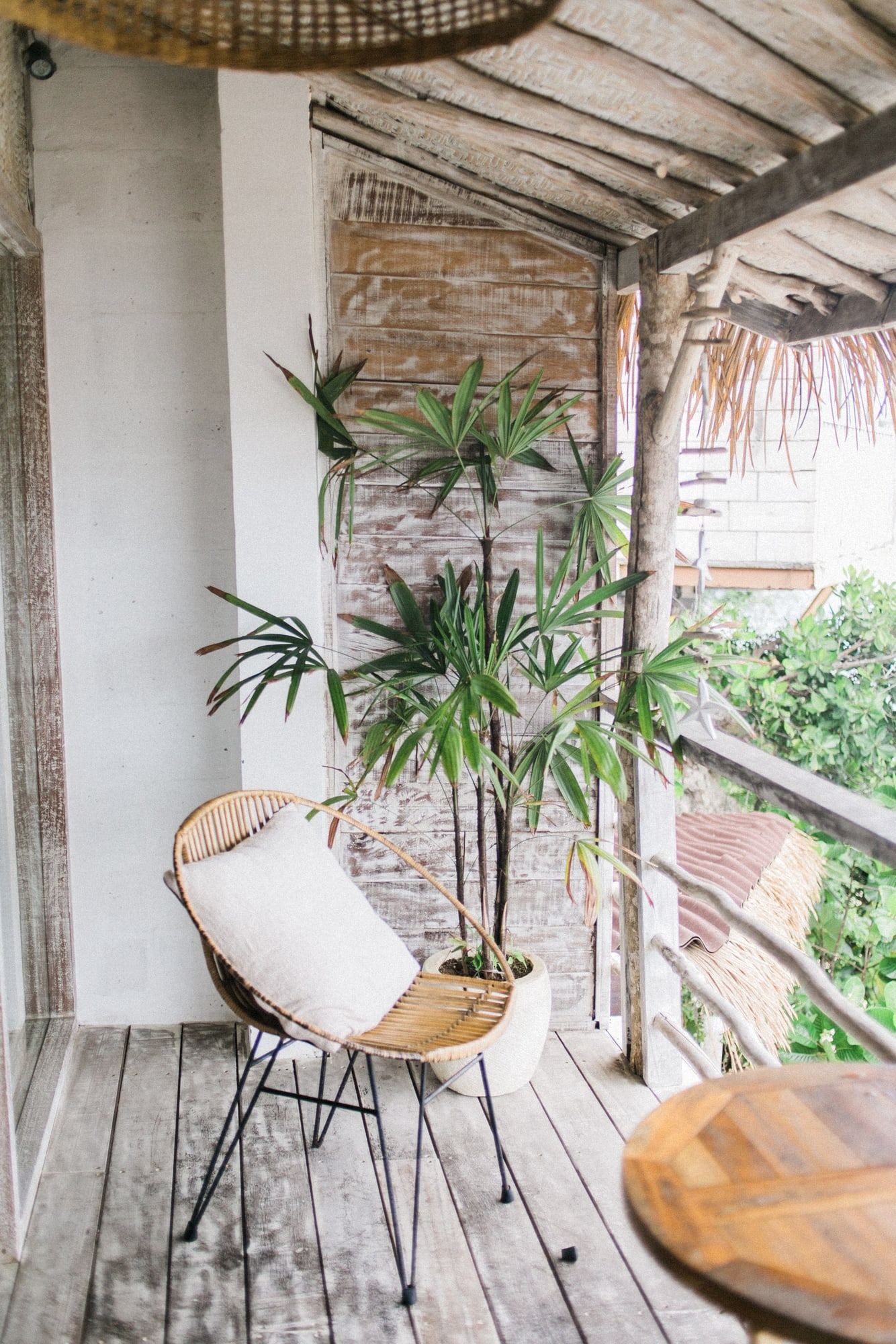 La terrasse : un plancher de bois, un fauteuil en rotin et des palmiers en pot